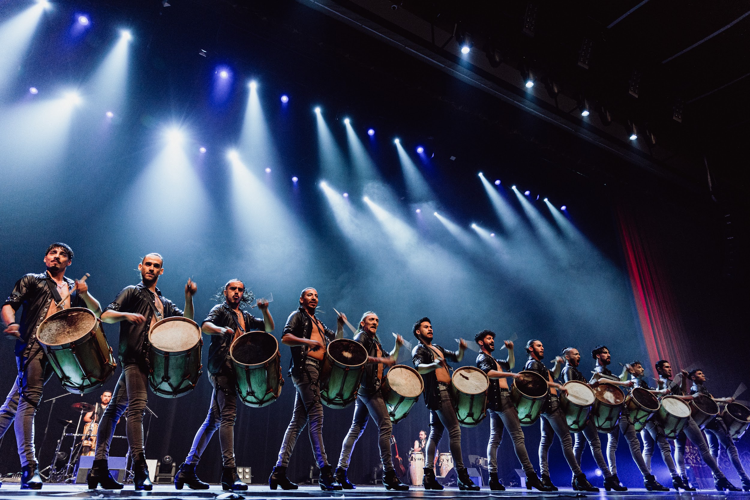 all male drummers in a line on stage, left legs in same stance