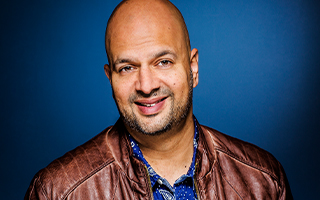 a smiling bald gentleman in a brown leather jacket, deep blue background