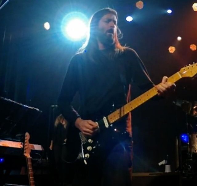 a guitarist on stage playing a guitar with a spotlight shining behind his head