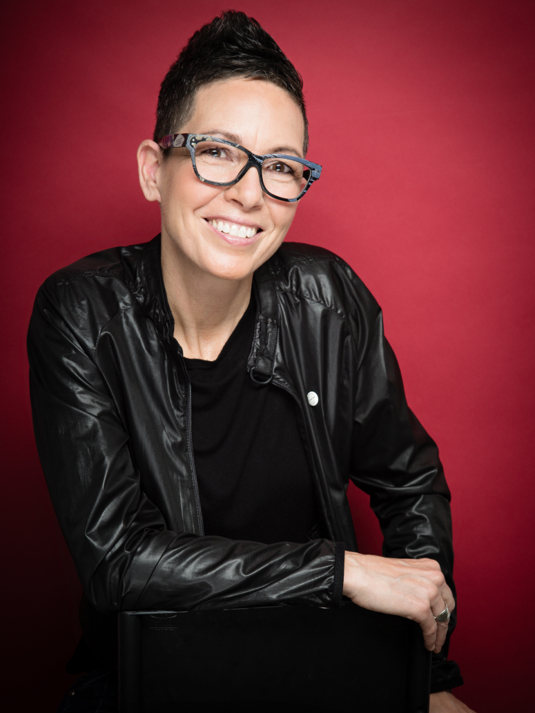 Headshot of Elvira Kurt in a black leather coat infront of a red background