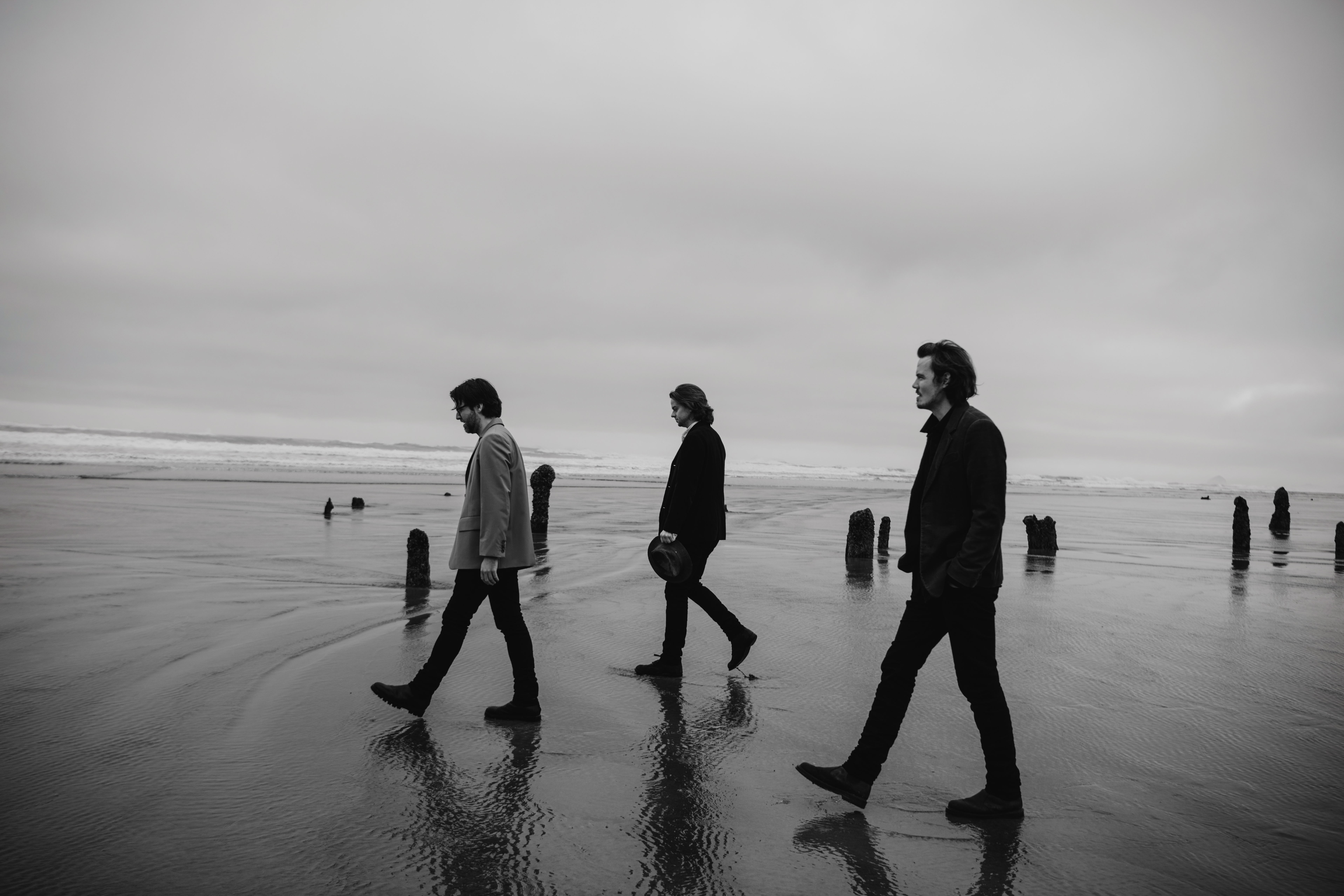 Black and white photo of the three band members walking on a beach