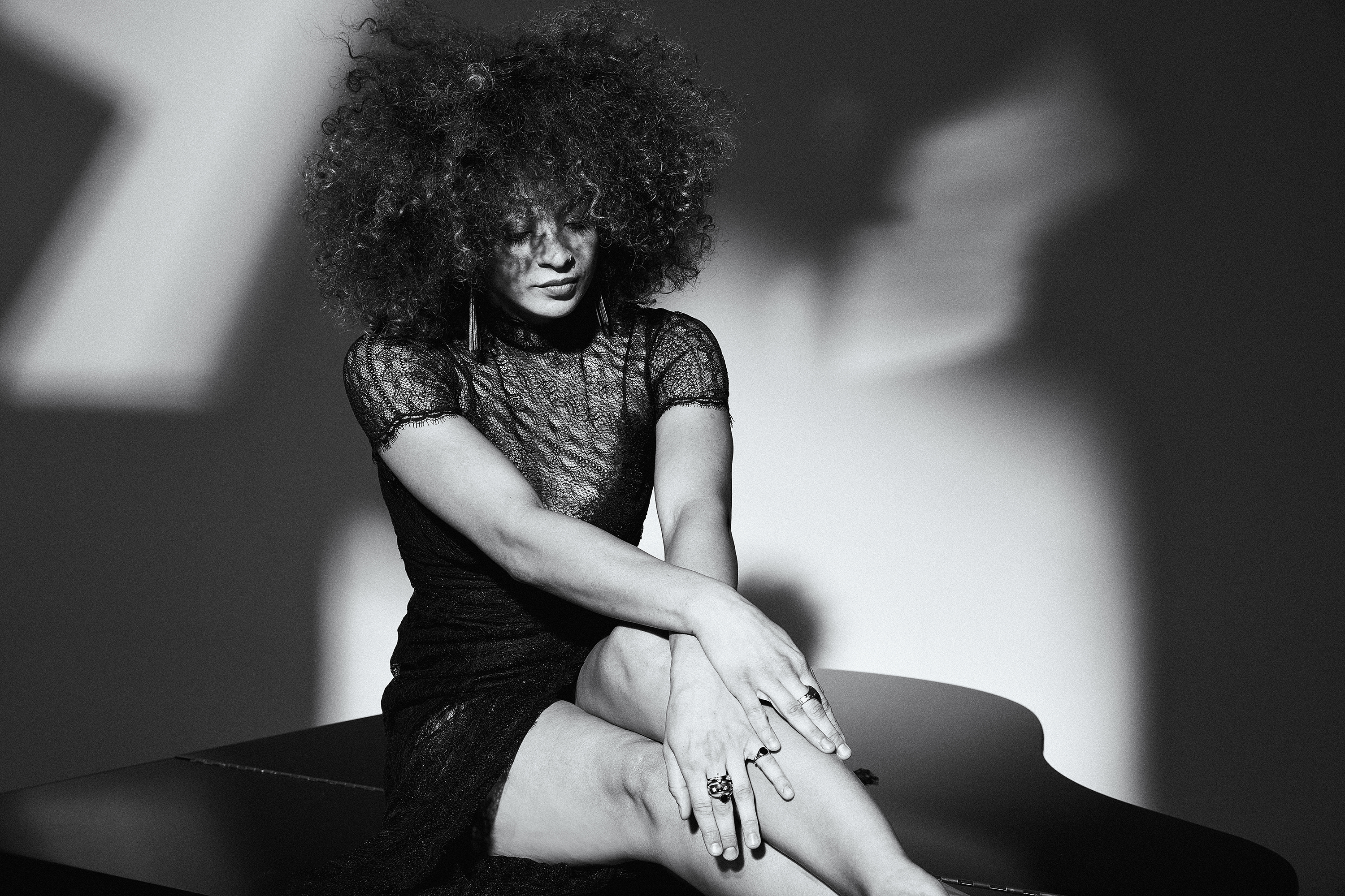 Kandace Springs, sitting with her legs crossed off the side of the piano, looking down