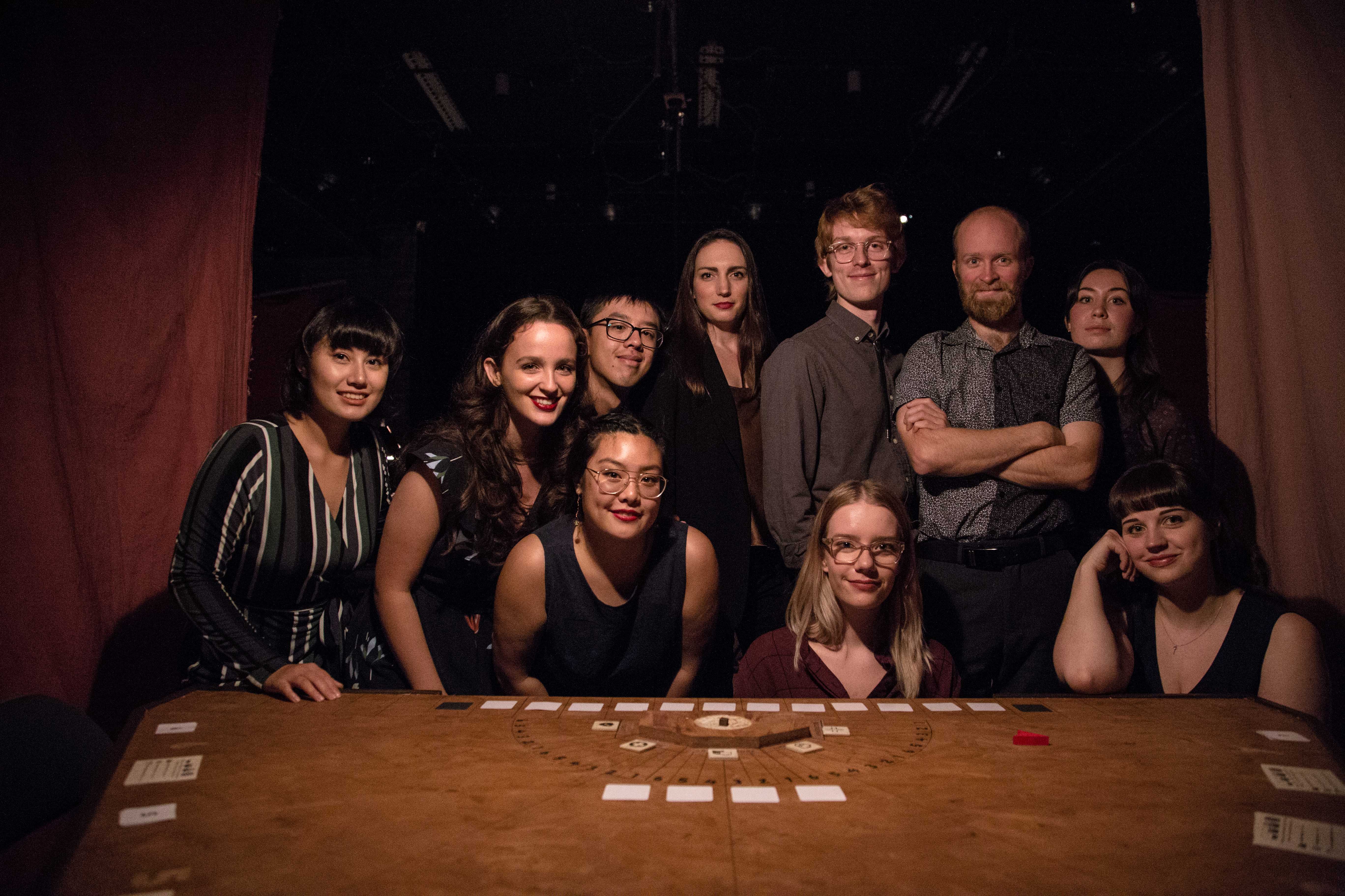 Performers around a table with cards