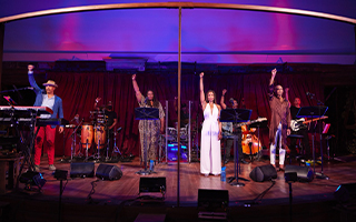 four performers on stage with their right arms raised