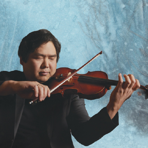 Alt text:  Violinist performing against a textured blue background, holding a violin and bow mid-performance.