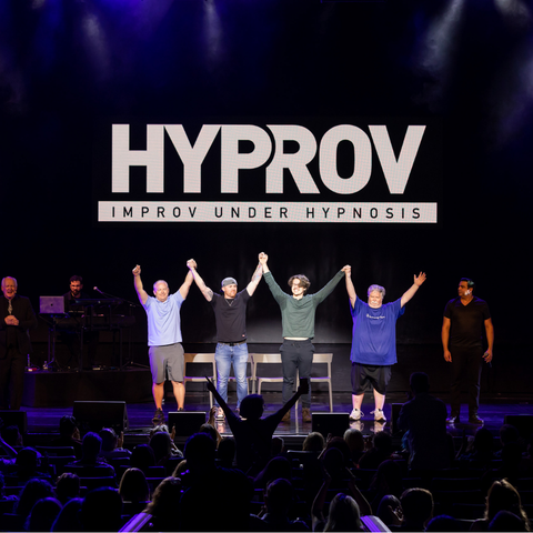 Four people standing on stage looking at the camera with their hands in the air