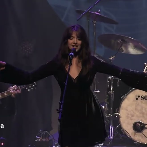 A person singing in a black dress with arms extended