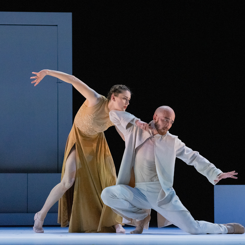 Two dancers, one in white and one in gold holding onto each other