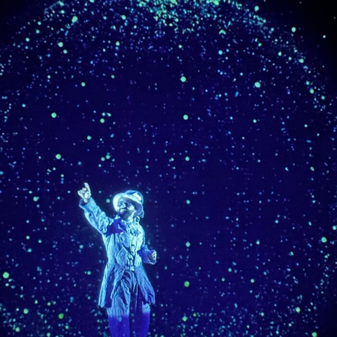 Actor pointing towards the ceiling all in shades of blue with stars