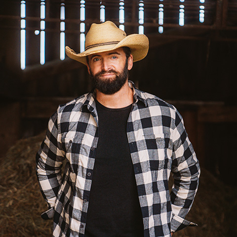 Dean Brody in brown cowboy hat and plaid shirt, hands in his pockets
