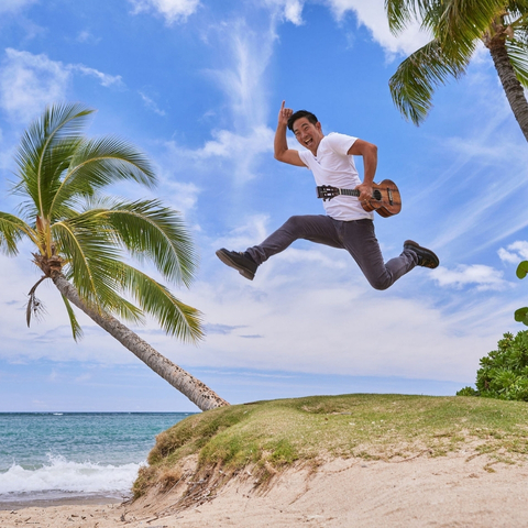 A man jumping on a beach holding a ukulele