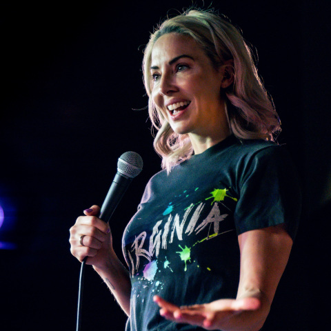 Whitney Cummings on stage with a micro phone in her right hand