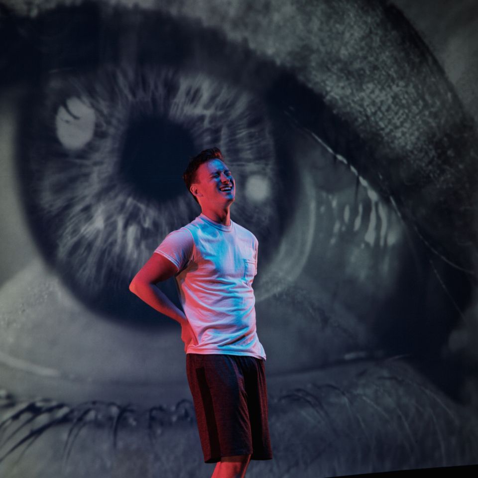 Love Me Forever Billy H. Tender actor in a white shirt infront of a giant black and white photo of an eyeball