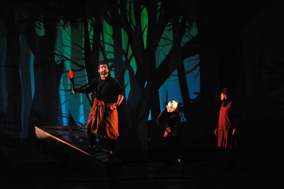 A young boy on stage standing in front of a forest set