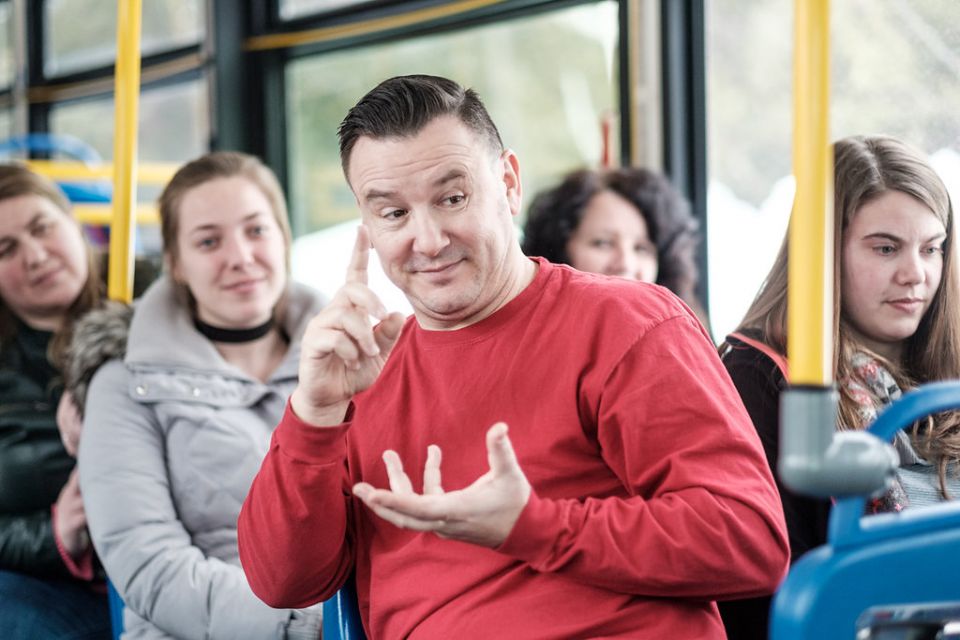 Tales of an Urban Indian actor in a red shirt sits on a public transit bus