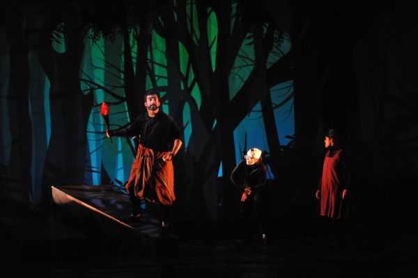 A young boy on stage standing in front of a forest set