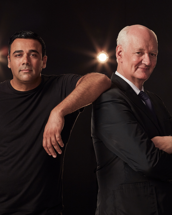 Asad Mecci and Colin Mochrie both in black stand looking at the camera
