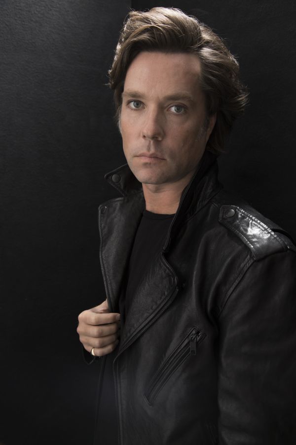 Rufus Wainwright posing in a black leather jacket. 