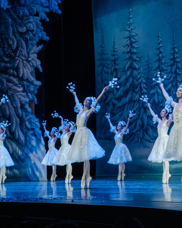 Ballerinas dressed in white on stage with arms raised in the air