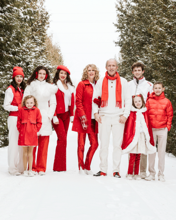 Natalie MacMaster, Donnell Leahy and family dressed in white and red poising for the camera outside with trees in the background 