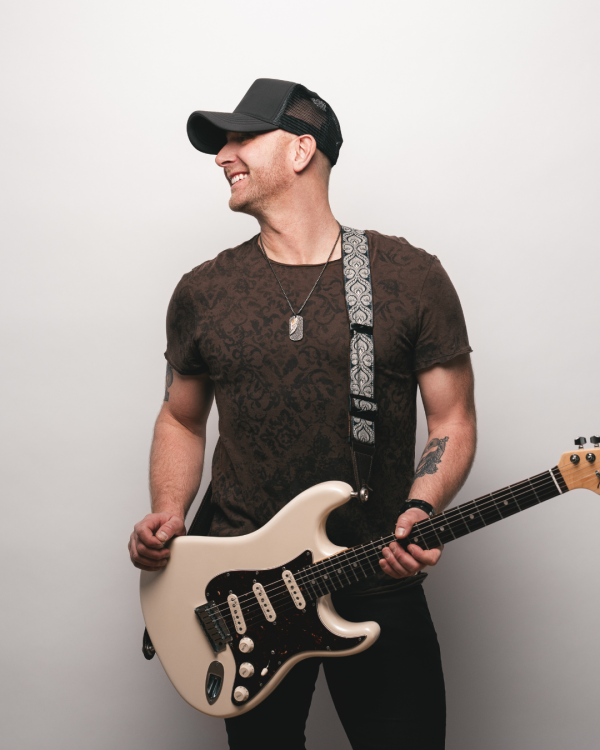Tim Hicks holding a guitar looking off to the left.