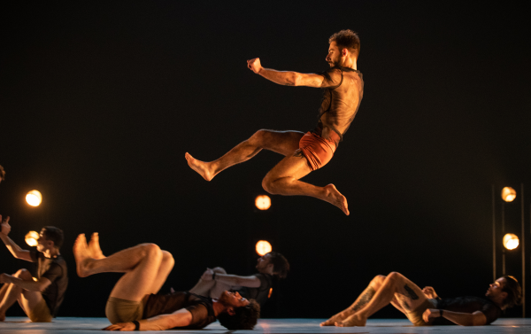 A performing jumping mid-air over other performers on stage