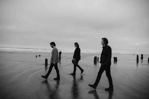 Black and white photo of the three band members walking on a beach