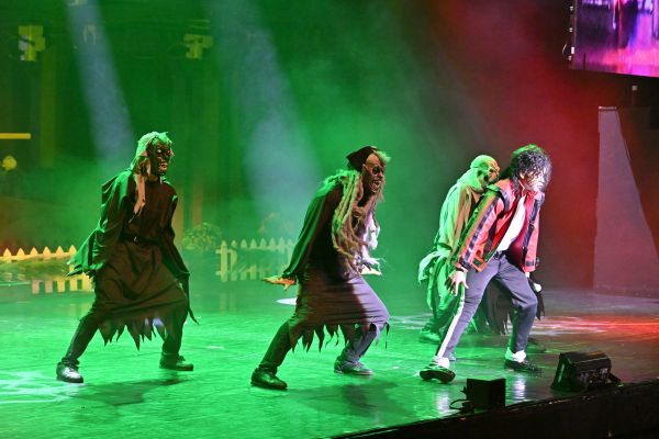 performer on a green lit stage with zombies dancinf behind him