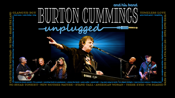 Burton Cummings on stage, singing into a microphone with his arm in the air