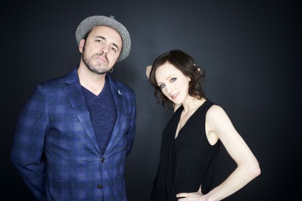 Sarah Slean and Hawksley Workman in blue, in front of a dark grey wall