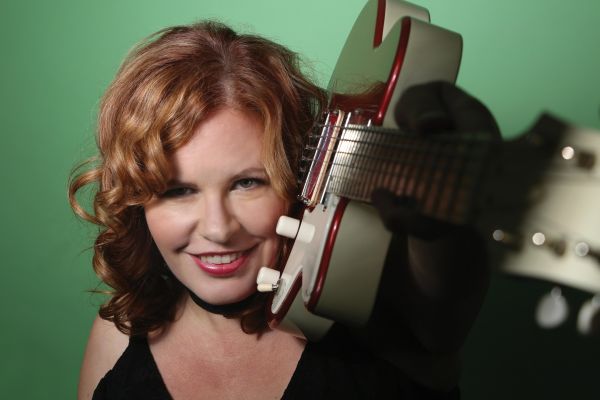 Photo of Suzie Vinnick with an electric guitar on her shoulder.