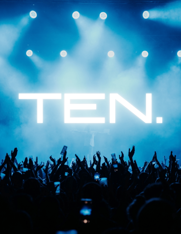 Concert crowd with raised hands in front of a stage lit blue, with the word ‘TEN.’ displayed in large white letters.