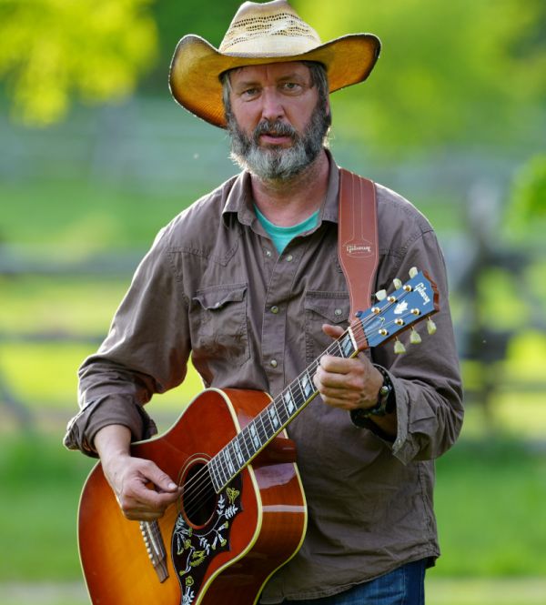 bearded man with a guitar, wearing a hat with a green background