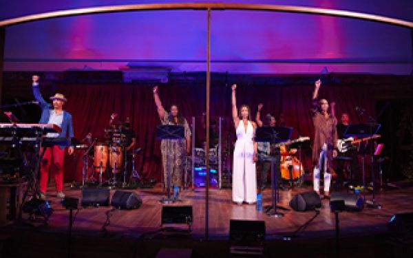 four performers on stage with their right arms raised